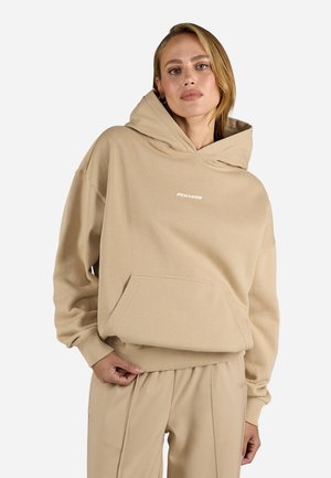 Beige oversize hoodie gjord av mjukt tyg, med en stor huva, framficka och tryckt logotyp. Ribbad mudd och fåll.