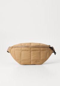 Quilted tan fanny pack with a zipper closure, featuring a slightly curved shape and textured padded surface. Adjustable strap included.