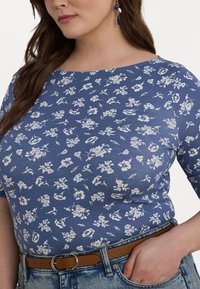 Blå blomstermønstret topp med trekvart ermer, rund hals, og en glatt tekstur, kombinert med høyt liv denim og et brunt belte.