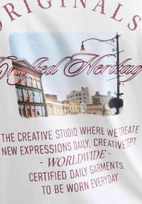 T-shirt bianco con stampa grafica di un paesaggio urbano e testo in rosso scuro, che mostra uno stile vintage e una texture leggermente sbiadita.