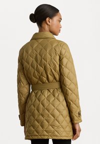 Gequilte lange jas in olijfgroen, met een ceintuur in de taille, kraag en knoopmanchetten. Zachte textuur met een ruitpatroon over de gehele jas.