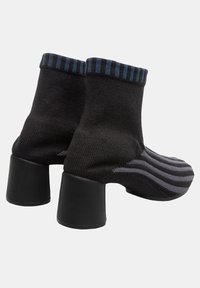 Black knit heeled boots with a fitted ankle design, featuring a blue-and-black striped collar and a block heel. Striped pattern at the toe.
