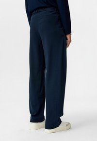 Marineblauwe wijde broek met een gladde textuur, voorzien van een tailleband, achterzak en een losse pasvorm, gecombineerd met witte sneakers.