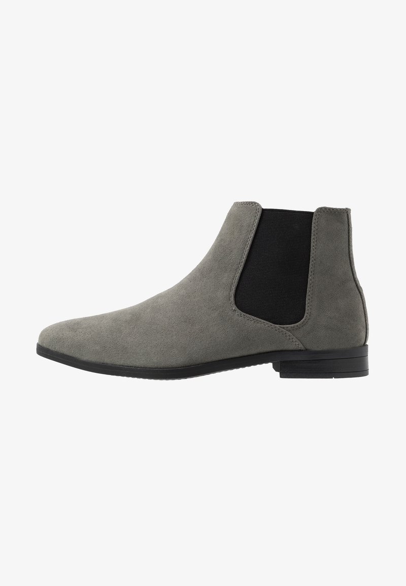 Bottine Chelsea en daim gris avec un panneau latéral élastique noir et un petit talon noir, visible de profil droit sur fond blanc.