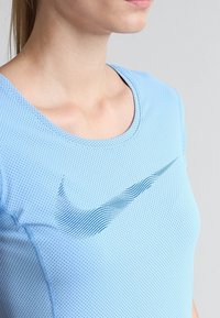 Camiseta deportiva de manga corta en azul claro, hecha de tela transpirable, con un patrón de malla texturizada y un logo de Nike en azul oscuro en el pecho.
