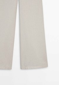 Pantalon beige à jambes larges avec ourlets visibles, présenté de la moitié de la cuisse jusqu’aux chevilles sur fond blanc.