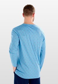 Himmelblaues Langarmshirt mit einem Allover-Diamantmuster in Dunkelblau und Rot. Sanfte Textur mit lockerem Schnitt und rundem Ausschnitt.