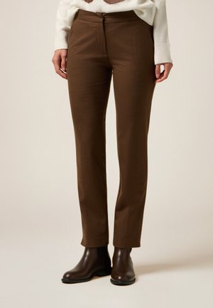 Brązowe, dopasowane spodnie o fakturze, noszone z ciemnobrązowymi botkami za kostkę i białym swetrem, pokazane od połowy uda do stóp na jednolitym tle.