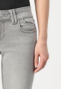 Grå denimjeans med en glatt tekstur, høy midje, beltehemper og frontlommer. Sømmen er synlig langs sømmene.