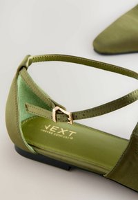 Zapato plano de satén verde con punta afilada, correa en el tobillo y detalle de hebilla dorada. Cuenta con una plantilla suave verde y suela negra.