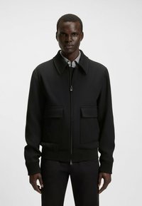Veste bomber noire avec fermeture éclair à l'avant, grandes poches avant, poignets et ourlet côtelés, fabriquée dans un tissu lisse et structuré.