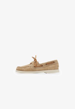 Zapato de barco de gamuza beige con suela de goma blanca, detalles en cuero, cordones decorativos y costura a lo largo del borde.