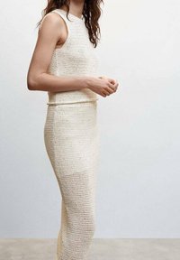 Ensemble robe en maille couleur crème comprenant un haut sans manches et une jupe ajustée, avec une texture à tissage ouvert et un design sans coutures.