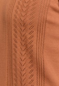 Roestkleurige gebreide stof met een gestructureerd, zigzagpatroon en openwerkdetails aan één kant, wat visuele interesse en diepte creëert.