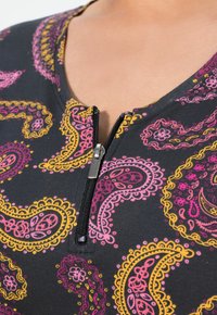 Schwarzes Kleidungsstück mit einem Reißverschluss am Ausschnitt. Der Stoff zeigt ein Paisleymuster in Pink-, Lila- und Gelbtönen.