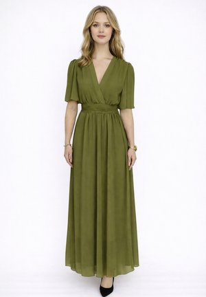 Donna che indossa un abito lungo verde oliva, a maniche corte, con scollo a V e vita aderente, in piedi su sfondo bianco semplice.