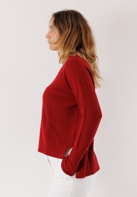 Maglione rosso con dettagli a costine, spacchi laterali e un fit comodo. Realizzato in tessuto morbido, presenta maniche lunghe e un orlo arrotondato.