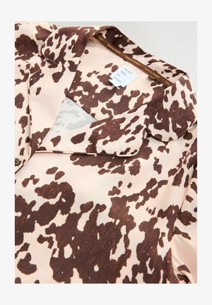 Bluză cu pete maronii și crem, cu o textura moale și mătăsoasă, având un guler și un eticheta în interior care spune "NEXT time to dream."