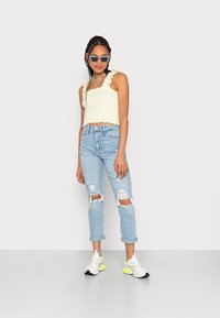Top cropped amarelo claro com bordas de babados, combinado com jeans rasgados azul claro. Usado com ténis brancos e amarelos e óculos de sol.