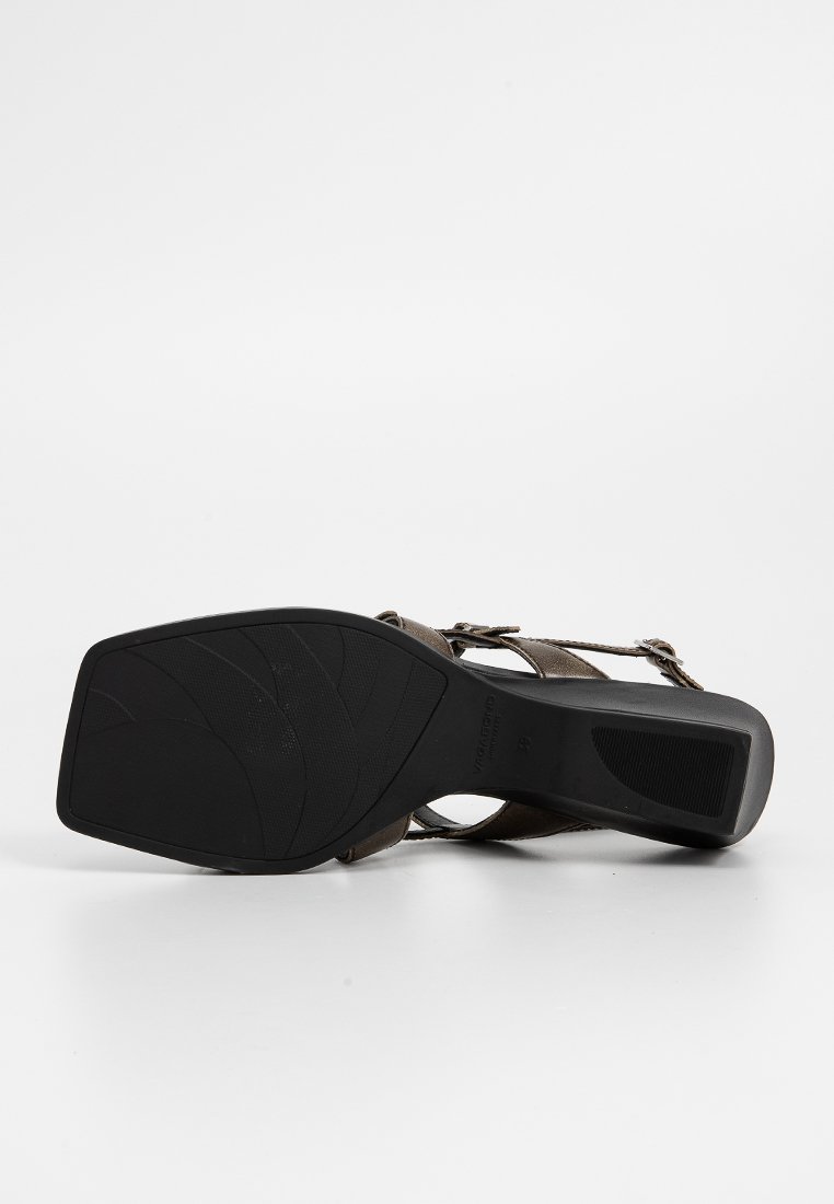 Sandale à talons brune avec une semelle en caoutchouc noir texturé, présentant des brides en cuir et une fermeture à boucles. Le design est à bout ouvert et strappé.