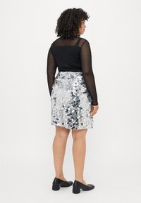 Top negro de manga larga transparente combinado con una falda de lentejuelas plateadas. La falda cuenta con una cintura ajustada y una forma acampanada, acentuada con lentejuelas reflectantes.