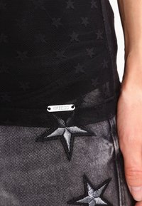 Top de malla negra con patrón de estrellas, que presenta una etiqueta de logo plateada. Combinado con denim gris, acentuado con estrellas bordadas en negro y plata.