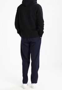 Svart huva sweatshirt i kombination med marinblå randiga byxor och vita sneakers. Tyget verkar mjukt, med en avslappnad passform i byxorna.