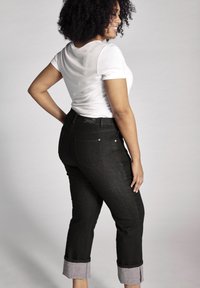 Juodi džinsai su sukta apačia, aukštu liemeniu, dviem galiniais kišenėmis ir subtiliu siūlų raštu. Derinami su balta marškinėliais.