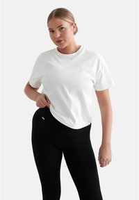 Vit bomull T-shirt med rund hals och korta ärmar, matchad med svarta ribbade leggings. T-shirten har subtil märkning nära halsringningen.