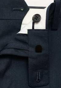 Cintura de pantalones de traje azul marino oscuro mostrando el botón, el ojal y el cierre de gancho y barra negro sobre el forro blanco.
