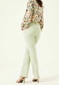 Jeans alta vita verde menta con design a gamba dritta, dotati di due tasche posteriori e dettagli di cucitura discreti. Indossati con una blusa a fantasia.