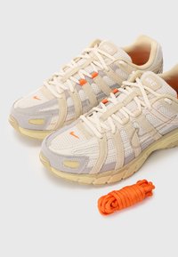 Beige og grå Nike-sneakers har et mesh-overdel med tekstilakenter, tykk såle og oransje detaljer; inkluderer et ekstra sett med oransje lissser.
