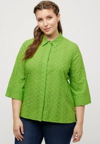 Blusa verde colletto con maniche a tre quarti, caratterizzata da ricami ad occhio in un motivo a diamante e una linea dritta.