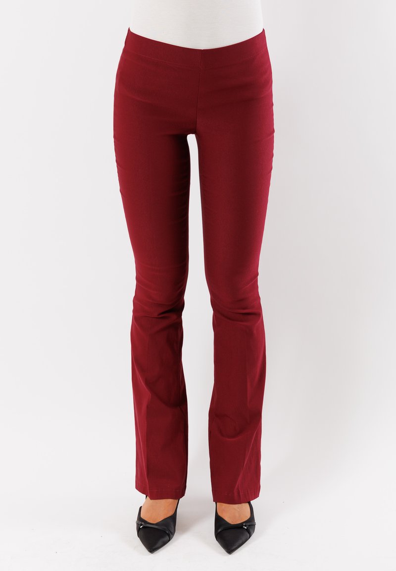 Pantaloni fitted bordeaux con una texture liscia, gambe svasate e vita alta, abbinati a scarpe nere a punta.