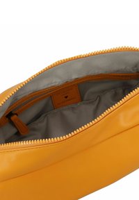 Sac en cuir jaune avec une fermeture éclair, doté d'un intérieur en tissu gris et d'une poche zippée intérieure. L'étiquette à l'intérieur indique "Conçu avec ❤️ en Allemagne."