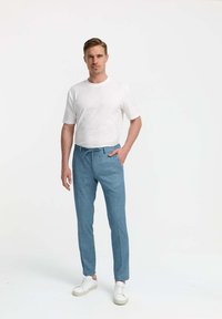 Light blue tailored trousers with a drawstring, paired with a plain white short-sleeve t-shirt and white sneakers, standing against a plain background.