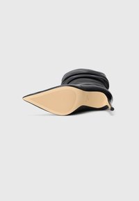 Schwarze Leder-Stiefelette mit spitzem Zehenbereich, die auf der Seite liegt und eine beigefarbene Sohle mit strukturierter Rutschfestigkeit sowie einem lässigen Oberdesign zeigt.