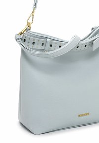 hele sinine nahast käekott, millel on sile pind, kaunistatud mustrilise rihmaga koos kuldsete detailidega ja väikese logoga põhjaosas.