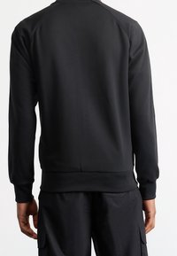 Svart sweatshirt med rund halsringning och ribbade ärmslut. Har en slät yta och en enkel, klassisk design utan synliga logotyper eller dekorationer.