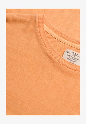 T-shirt a girocollo di colore arancione chiaro con etichetta del marchio Superdry visibile cucita all'interno del colletto.