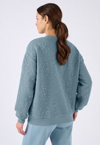 Sudadera texturizada de color azul claro con patrón floral, cuello redondo y puños y dobladillo acanalados. Vista trasera que muestra un diseño de corte relajado.