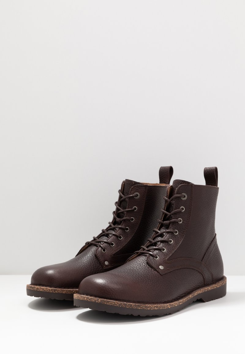 Braune Leder-Ankle-Boots mit strukturiertem Finish, Schnürdesign und einer braunen Gummisohle mit einem leichten Korkakzent.