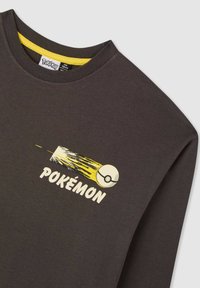 Ciemnoszary t-shirt z długim rękawem z żółtym dekoltem. Posiada grafikę Pokémon z Pokéball'em oraz liniami ruchu w kolorze żółtym i białym.