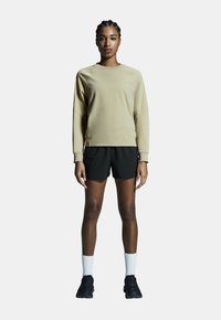 Beige langemouwen top met raglanmouwen, gecombineerd met zwarte shorts. Gekleed met witte crew sokken en zwarte sportschoenen.