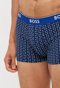 Boxeri scurți cu un model albastru, prezentând un design geometric, o textură moale și o talie elastică cu logo-ul "BOSS" în alb.