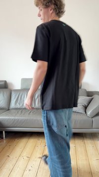 Camiseta preta de manga curta com corte descontraído, feita de algodão, apresentando um logótipo subtil nas costas, combinada com jeans azuis em denim.