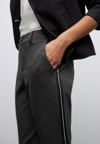 Graue Hose aus strukturiertem Stoff in Slim-Fit-Passform, mit Seitentaschen und einem schwarzen Streifenakzent entlang der Länge.