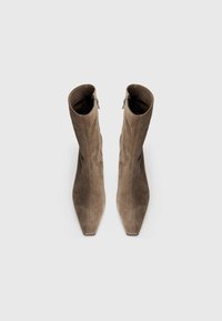 Bottes ankle en suède marron avec un bout pointu, texture lisse et fermetures à glissière latérales. La tige présente un design structuré et une forme légèrement décontractée.
