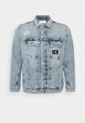 Veste en jean bleu clair délavée avec fermeture à boutons, deux poches poitrine et un petit patch noir avec le logo Calvin Klein sur la poche droite.