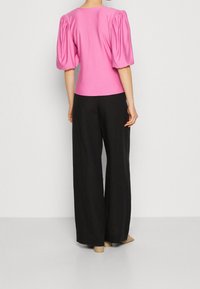 Růžový top s balónovými rukávy a kulatým výstřihem, doplněný o volné široké černé kalhoty. Hladký pocit na dotek, minimalistický design bez viditelných vzorů.